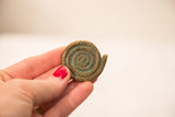 Handheld vintage bronze coiled snake gold weight showing aged patina and textured lines.