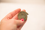 Textured bronze coiled snake gold weight with historic patina, held in hand.