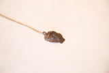 Vintage African pendant in profile, detailing its handmade texture and dark bronze patina.