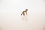 Three-quarter view of the small, handcrafted bronze lion, highlighting its slender legs and tail.