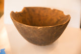 The rough, hand-carved texture and irregular chipped rim of a vintage wooden bowl.