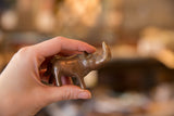 A vintage copper rhino sculpture held in hand, showing its small size and rich patina.