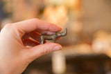 Miniature curved bronze rhino held in hand, showing side profile and dark patina.