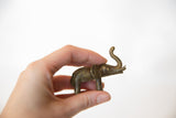 Collectible vintage African bronze elephant held in hand, showcasing raised trunk and aged patina.