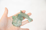Vintage copper fish pendant held in hand, showing its sculpted form and green patina.