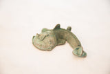 Side profile view of a vintage copper fish pendant showing its textured, green patina.