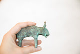 A hand holds the vintage copper bull, highlighting its small size and green patina.