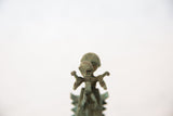 Detailed child figure in aged, green-brown oxidized copper with outstretched arms.