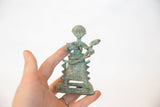 Oxidized copper figurine base, held in hand, with textured green patina.