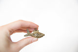Vintage bronze fish pendant held between fingers showing its size and patina.