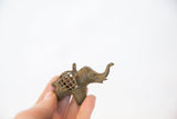 Profile view of a vintage bronze elephant pendant showing its textured mesh body and raised trunk.