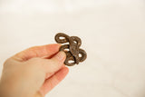 Hand holds the vintage African iron twisty snake, showing its dark, textured finish.