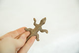 A vintage African bronze lizard held in hand, showing the handmade striped texture.