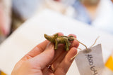 A hand holding the small vintage African bronze boar pendant with its item tag.