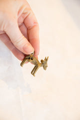A small, vintage bronze impala pendant held in hand, showing its textured surface.