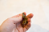 Small bronze sitting monkey pendant held between fingers, showing its vintage texture.