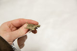 A hand holding the small vintage bronze turtle pendant to show its scale.