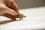A vintage bronze wire turtle pendant held between fingers, highlighting its small size.