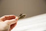 A hand holding a small, vintage bronze fish pendant with a textured mesh body.