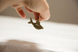 Vintage African bronze fish pendant with mesh design held in hand to show scale.