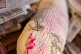 Vintage African bronze fish pendant with wire detail resting on a textured pink textile.