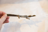 Slender profile and textured light patina of a vintage bronze crocodile shown in hand.