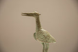 Aged, oxidized patina and coarse handmade texture on the bronze stork's head and neck.