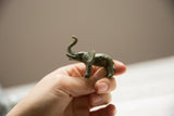 Small bronze elephant collectible held in hand, showing its side profile and patina.