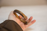 A hand holding the antique copper bracelet, showing its thick form and rich, aged patina.