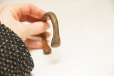 Close-up of the solid, flattened end and curved body of the antique bronze bracelet.