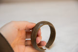 Hand holding vintage African bronze bracelet with intricate etched geometric patterns.