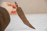A vintage iron chili pepper showing its heavily rusted patina and irregular handmade shape.