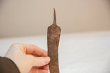 Hand holding vintage African iron chili pepper, revealing rustic texture and slight curve.