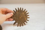 Hand holding a vintage African bronze sun medallion, showcasing its rustic, aged texture.