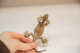 Hand holding the vintage African bronze gecko, showing its scale and aged gold patina.