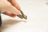 A hand holding the vintage African snake figure, detailing its textured head and body.