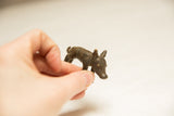 Hand holding a small, textured dark bronze pig figurine, showing its size.
