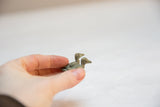 A hand holding the tiny pair of vintage African bronze sitting birds.