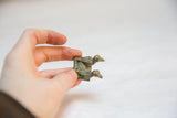 Small vintage bronze bird sculpture with a weathered patina held between two fingers.