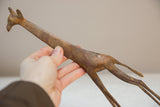 Hand holding the vintage African bronze giraffe, showing its light patina and spotted texture.