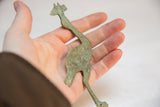 Vintage flat African metal stork with a weathered patina resting in a hand for scale.