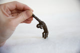 Textured dark bronze pangolin sculpture, its curved tail held by hand.