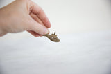 Hand holding vintage African bronze wire design fish pendant with textured scales.