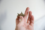 A hand holding a tiny African bronze fish pendant to show its scale and handmade texture.