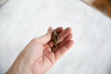 A small bronze fish pendant with an open mesh back held in a person's palm.