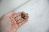 Vintage African mask pendant with oxidized bronze finish held in hand to show its scale.