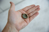 Small vintage bronze mask pendant's reverse, revealing time-softened green patina.