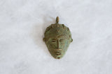Angled view of the vintage African bronze mask pendant showing its textured, oxidized surface.