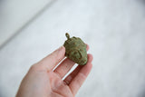 Vintage African bronze mask pendant held in hand to show its scale and handmade, oxidized texture.