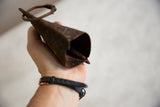 Hand gripping vintage African iron cow bell, showcasing its dark, textured patina.